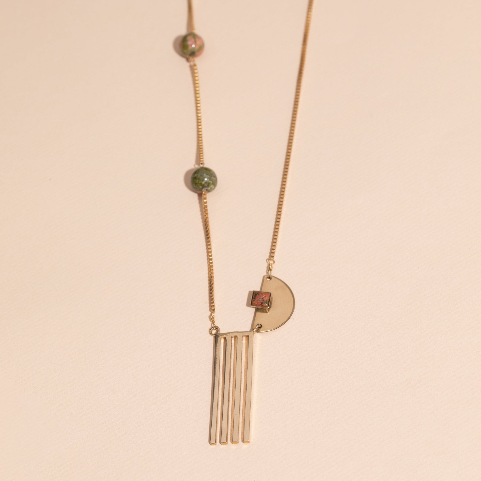 asymmetrical, brass box chain, three unakite beads, semi-circle with unakite square, four prong, brass pendant on bottom.